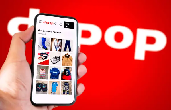 Hand holding a smartphone with the Depop app open and the Depop logo in the background