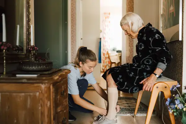 Female caregiver helping senior woman to put shoe at home