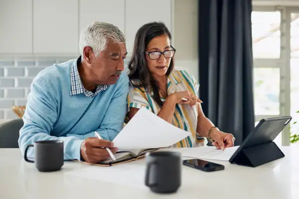 An elderly couple is sitting at their kitchen counter reviewing their finances.