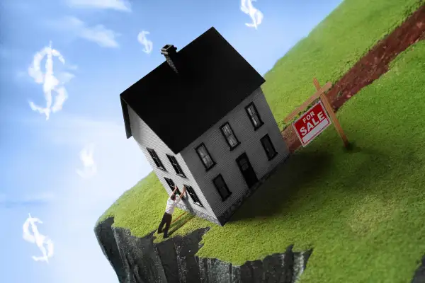 Man trying to prevent a house, for sale, from falling off a cliff.