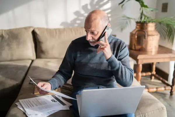 Senior man talking over the phone while looking at bills