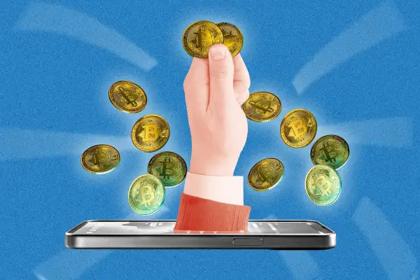 A hand coming out of a phone screen holding bitcoins