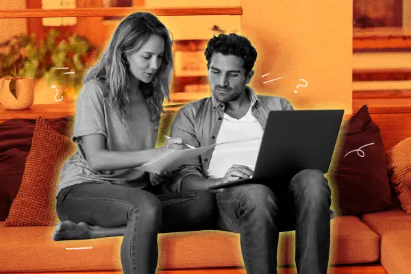 Couple sitting on their couch, looking at some documents while also using a laptop