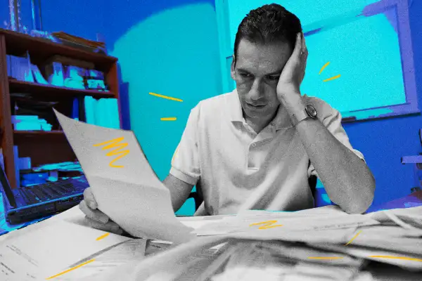 Worried man sitting at a desk looking over a lot of paperwork