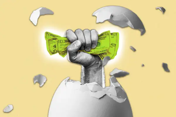 Hand holding money bursting through an egg shell